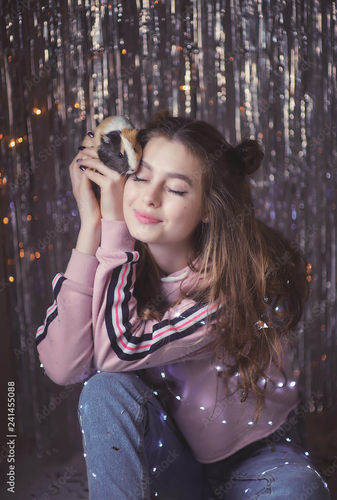 Fototapeta premium gentle and beautiful young girl on the background of garlands and tinsel with Guinea pig