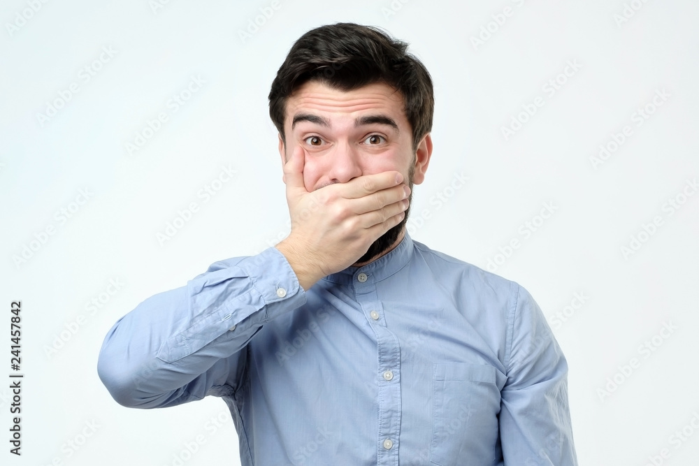 Good looking young man covering mouth with hand and looking at camera Good looking young man covering mouth with hand and looking at camera