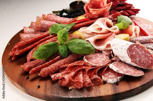 Food tray with delicious salami, pieces of sliced prosciutto crudo, sausage and basil. Meat platter with selection