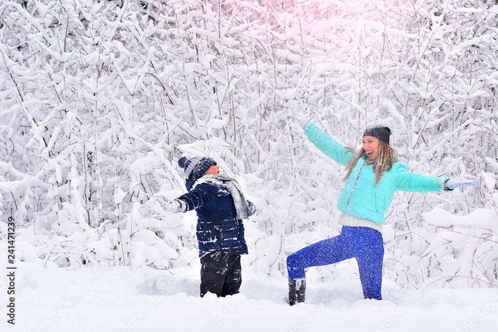 Mom and son throw snow up in a snowy winter park. Joy of life concept.