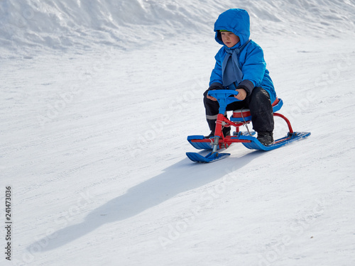 Boy in winter sledge rides on the mountain