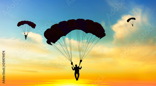 Silhouette parachutist landing at sunset