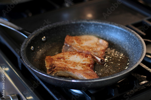 Pork chops frying in a pan on a stove top.
