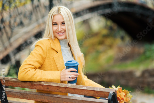 Young stylish blond woman drinking coffee to go in a park 