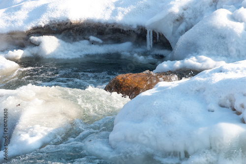 A detailed look at the water runs under the ice in the river. Snow melts from the mountains and flows in the creek