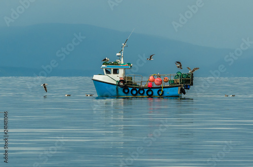 Small Fishing Boat With Lobster Pods And Seagulls On Calm Atlantic In Front Of The Hebride Islands