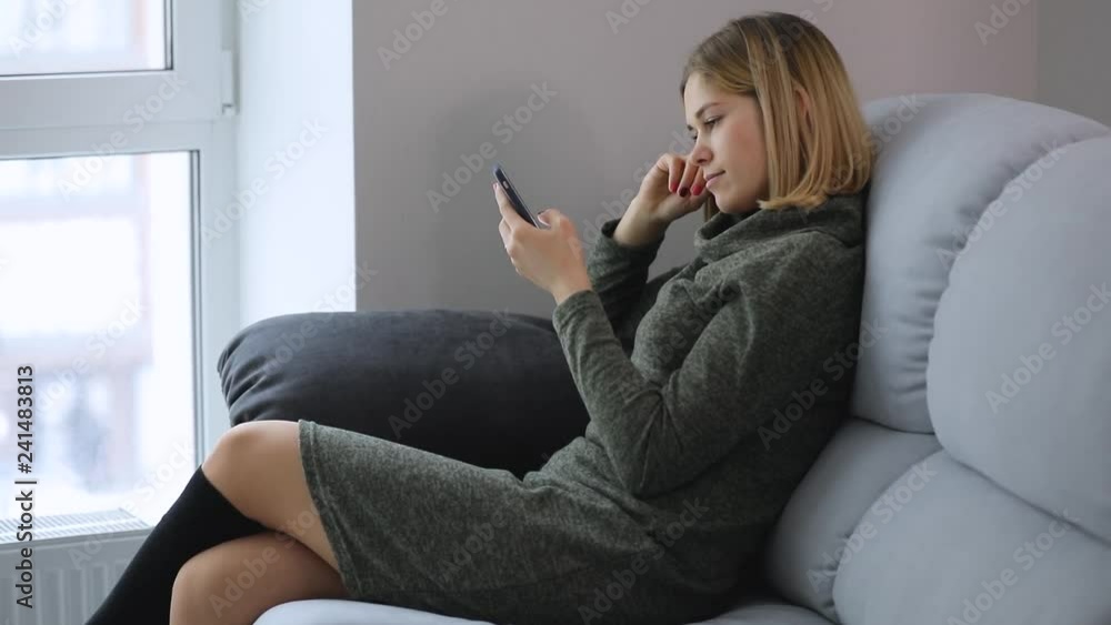 Woman browsing smartphone online in social site sitting on comfortable sofa at the home Woman browsing smartphone online in social site sitting on comfortable sofa at the home