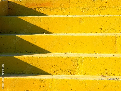Brightly lit yellow concrete staircase, with shadows on the left side