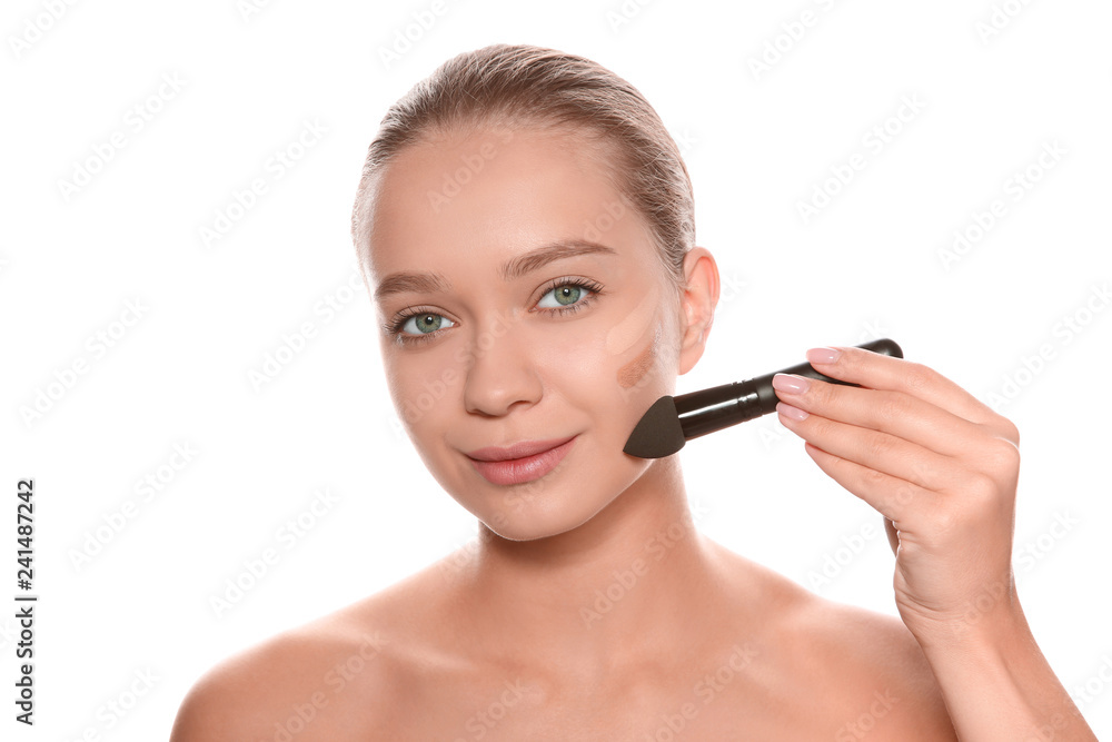 Young woman applying foundation on her face against white background