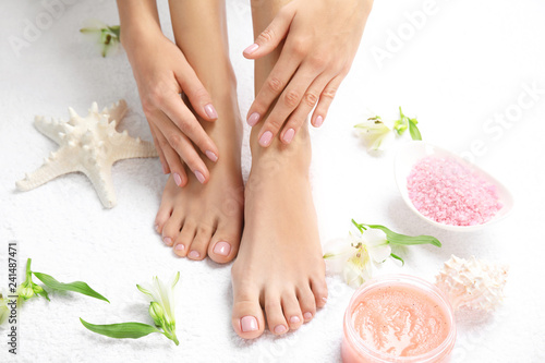 Cosmetic, flowers and woman touching her smooth feet on white towel, closeup. Spa treatment