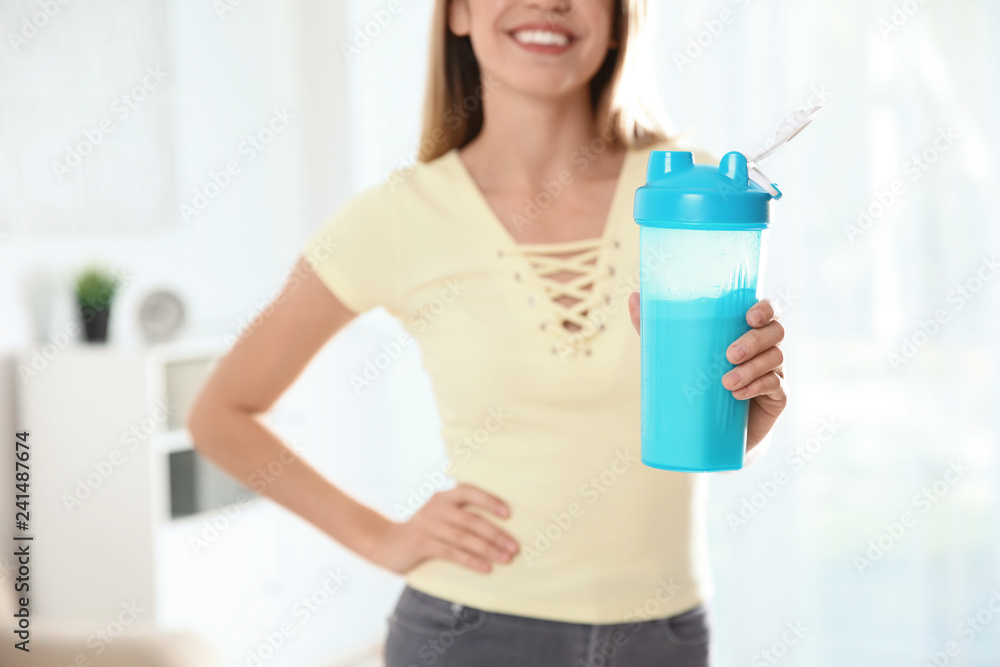 Young woman with bottle of protein shake at home, closeup