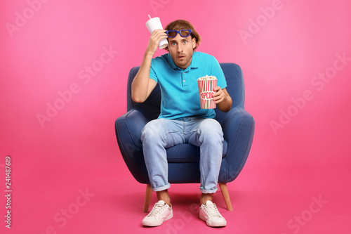 Emotional man with 3D glasses, popcorn and beverage sitting in armchair durin...