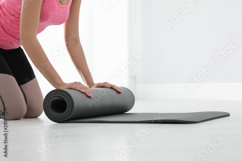 Young woman rolling yoga mat indoors, closeup. Space for text
