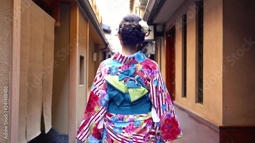 back view of young japanese girl in colorful kimono walking in path. female in traditional costume going to join festival in summer under sunshine. beautiful elegant lady in hanamikoji dori. photo