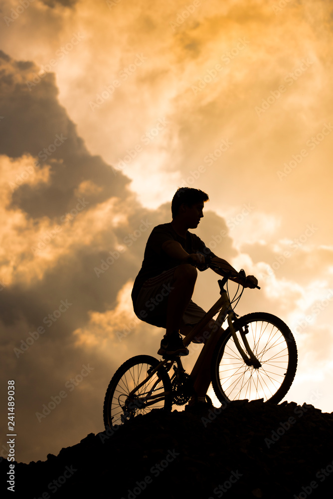 Obraz premium Silhouette of a boy riding a mountain bike at sunset