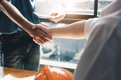 Engineers or architecture shaking hands at construction site for architectural project, holding safety helmet on their hands.