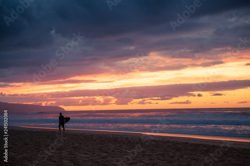 A surfer walks the beach after a sunset surf session on the North Shore of Oahu Hawaii
