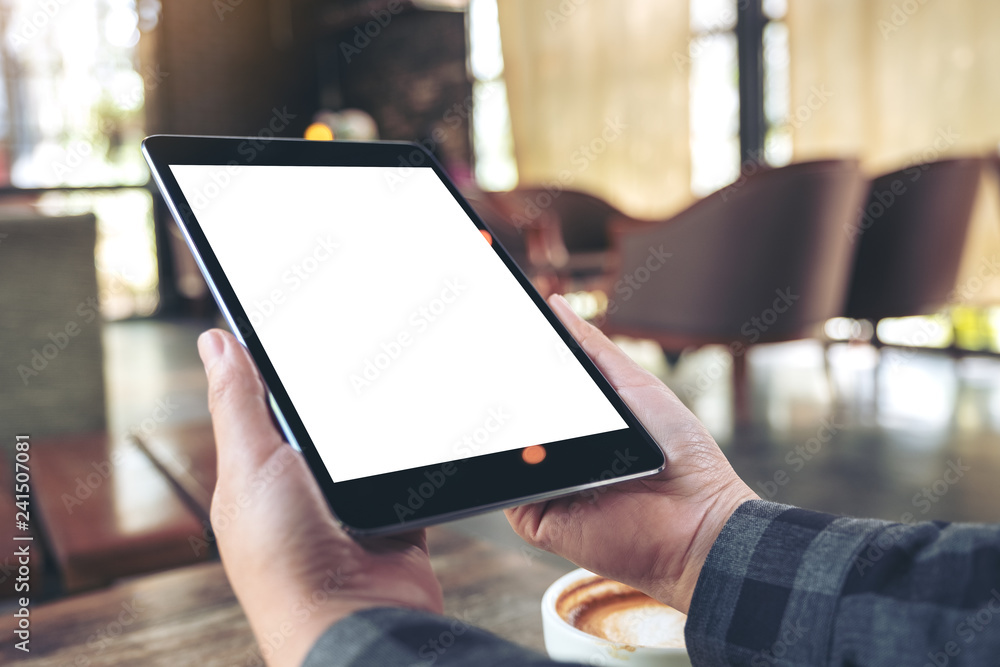 Mockup image of woman's hands holding black tablet pc with blank screen with coffee cup on wooden table in cafe