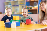 Cute woman and kids playing educational toys at kindergarten or nursery room