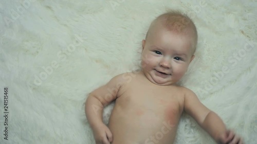 Five month old boy is lying on a blanket and smiles at the camera in slow motion.