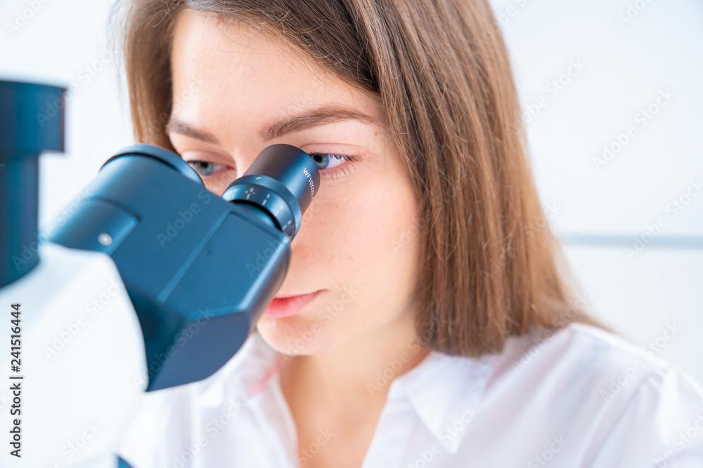 Young woman technician is examining a histological sample, a biopsy in the laboratory of cancer research Young woman technician is examining a histological sample, a biopsy in the laboratory of cancer research