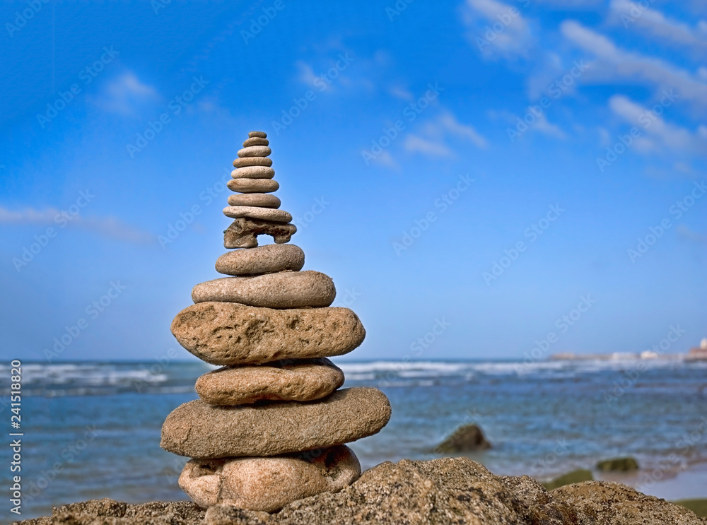 Fototapeta premium balanced stone cairn on a rock in front of ocean and blue sky