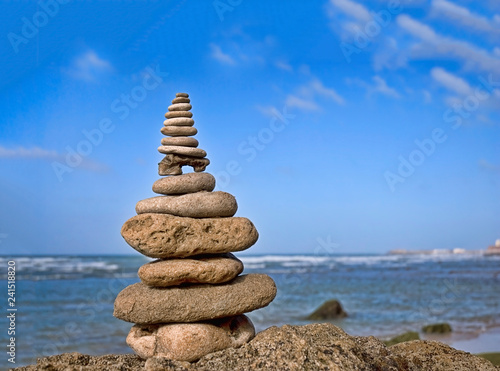 balanced stone cairn on a rock in front of ocean and blue sky