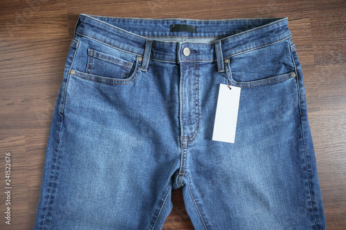 Blue jeans with blank white price label tag on wooden background