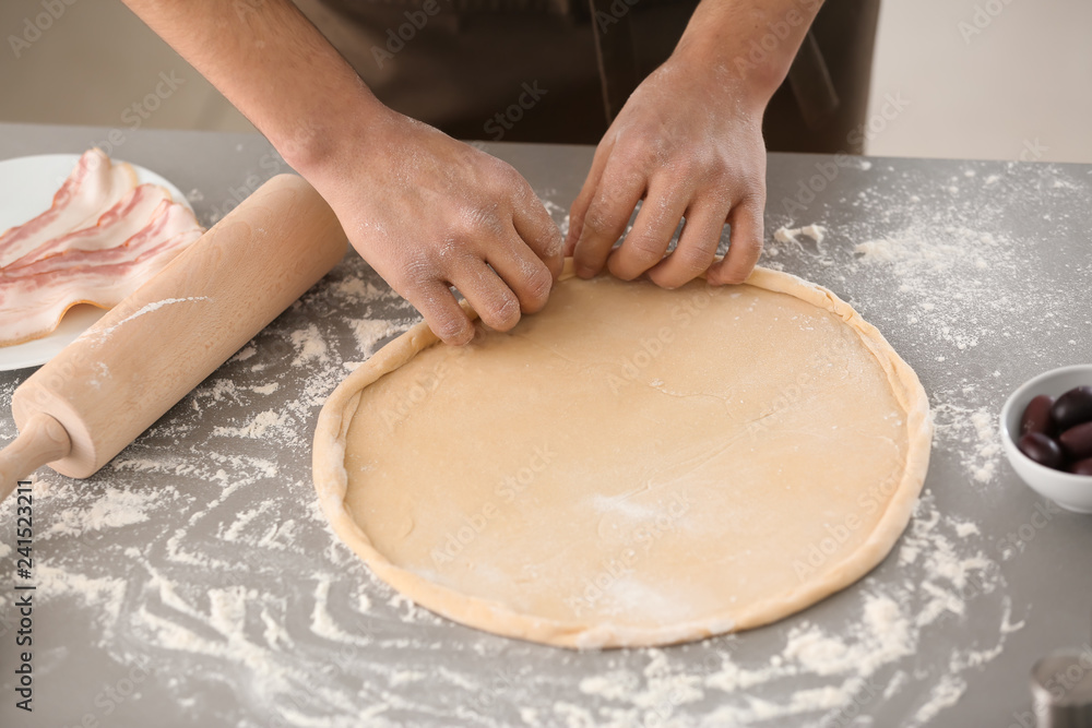 Fototapeta premium Young man preparing dough for pizza at table