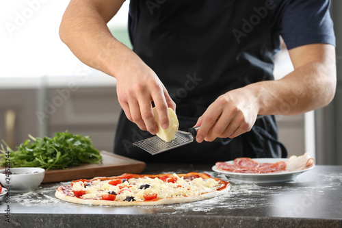 Young man preparing tasty pizza at table