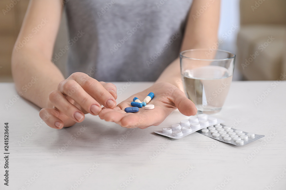 Young woman holding different pills at table, focus on hands