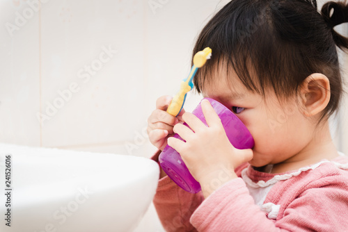 Sweet Asian child little girl brushing her teeth in bathroom
