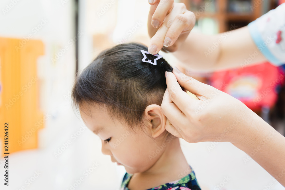 Fototapeta premium Asian lady weaving braids hair for Child little at home