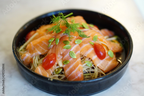 Raw sliced salmon meat on top of spicy Thai style papaya salad serving with fresh tomato and seed