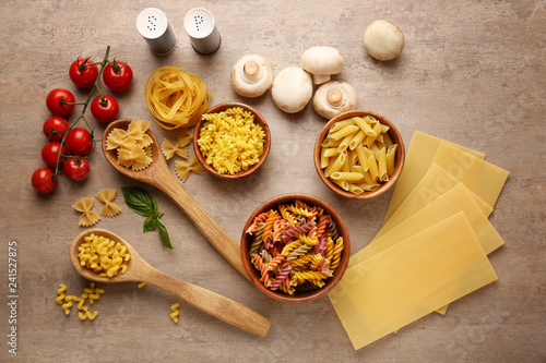 Different types of raw pasta with vegetables on wooden background