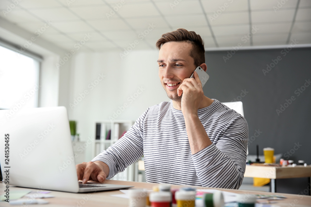 Young designer talking on mobile phone at workplace in office Young designer talking on mobile phone at workplace in office