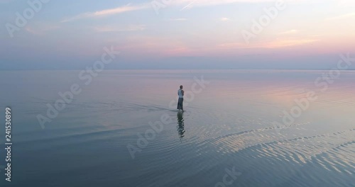 Beautiful dreaming woman walking in shallow reflecting sea water at sunset slow motion