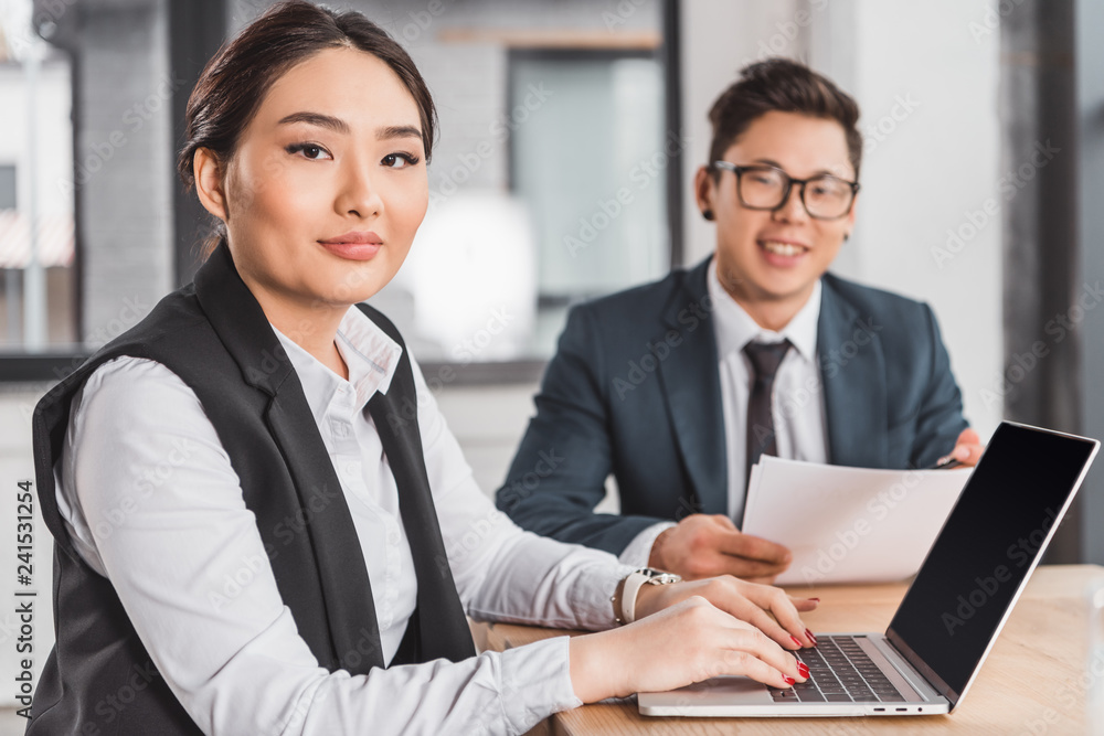 Obraz premium young asian business people smiling at camera while working with papers and laptop in office