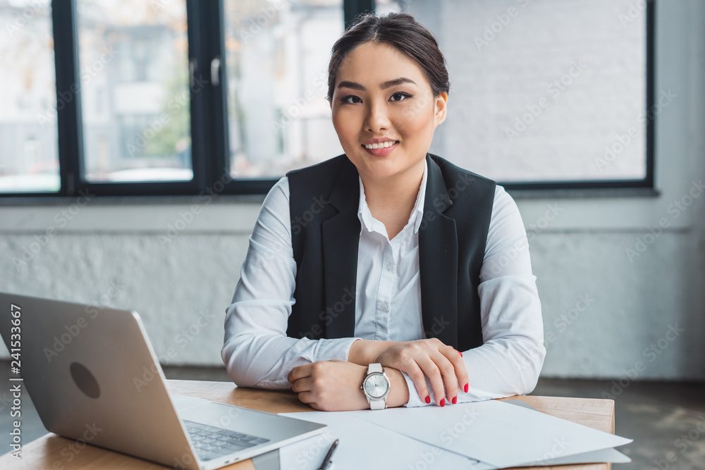 beautiful young kazakh businesswoman sitting at workplace and smiling at camera in office beautiful young kazakh businesswoman sitting at workplace and smiling at camera in office