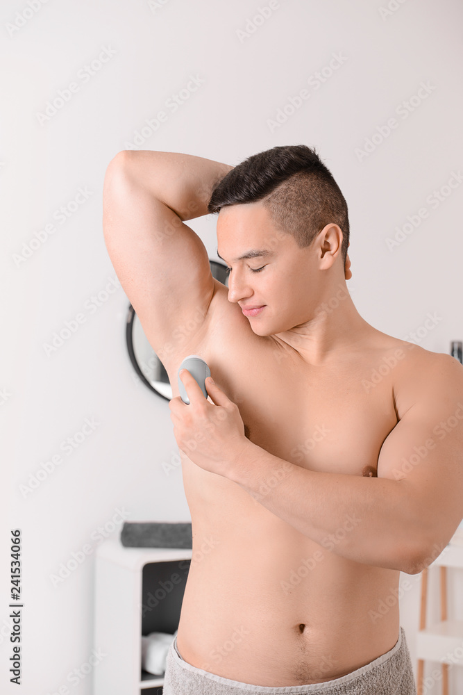 Obraz premium Young man using deodorant in bathroom