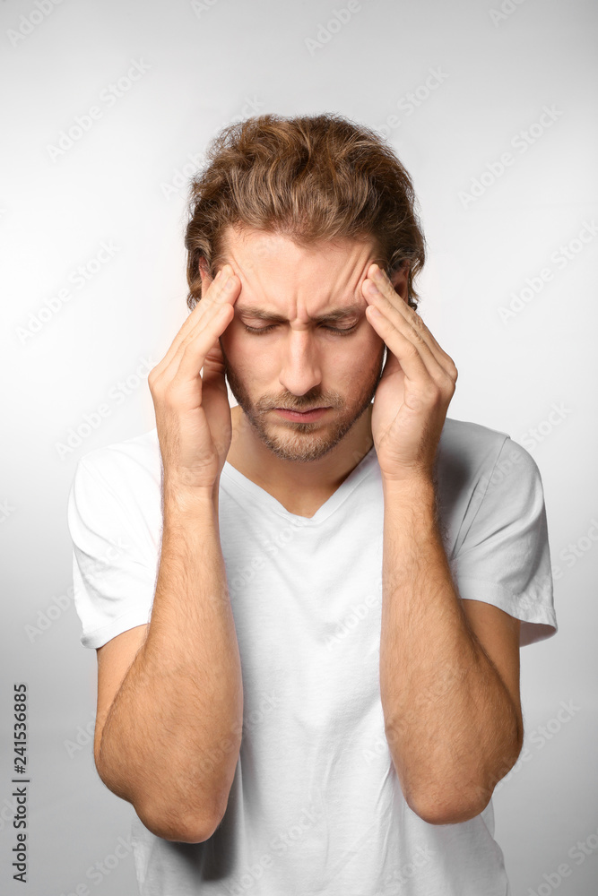 Young man suffering from headache on light background