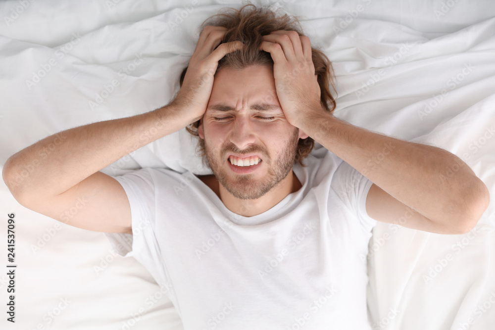 Young man suffering from headache in bedroom Young man suffering from headache in bedroom