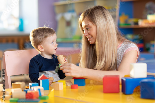 Cute woman and baby boy playing educational toys at creche or nursery