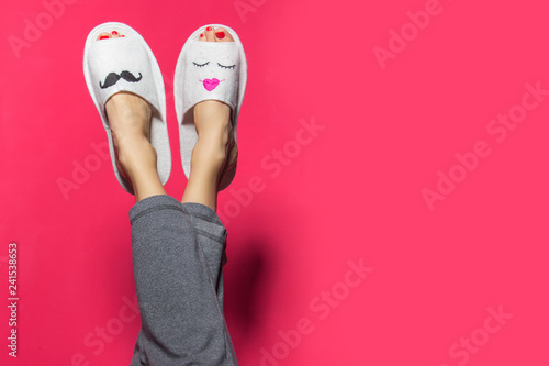 Cute funny couple on pink red. Woman wearing bright pants lying with legs upwards wearing unusual slippers with faces of man and woman photo