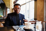 Fashionable african american man in suit and glasses sitting at cafe with cup of coffee.