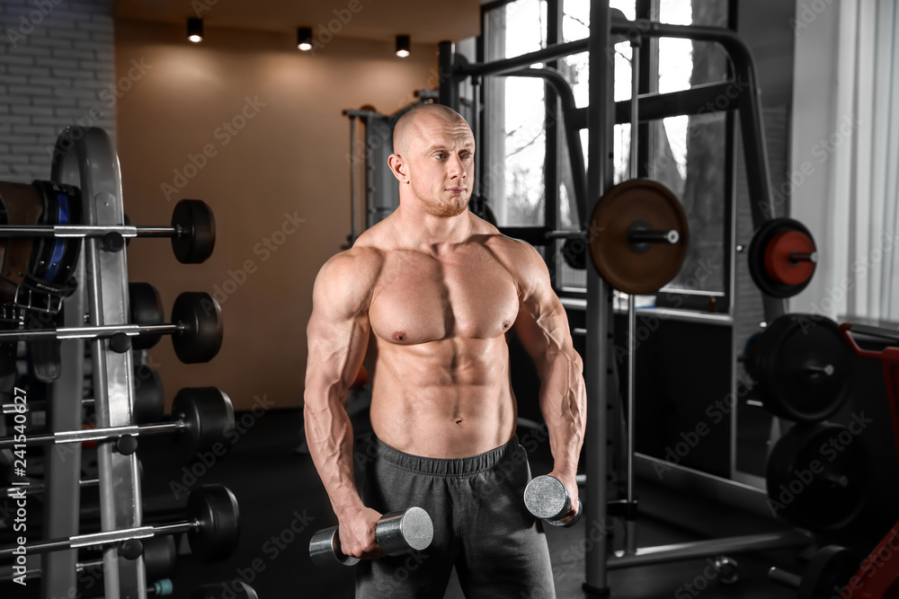 Fototapeta premium Muscular man training with dumbbells in gym