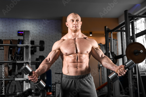 Muscular man training with dumbbells in gym