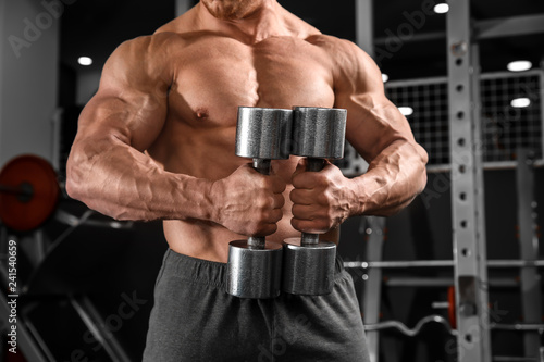 Muscular man training with dumbbells in gym