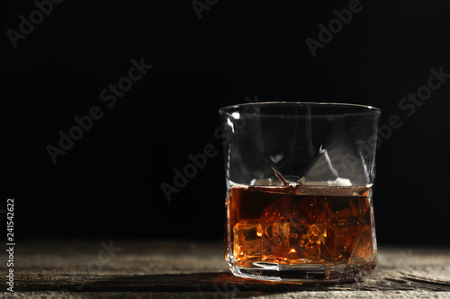 Glass of whiskey on wooden table against dark background