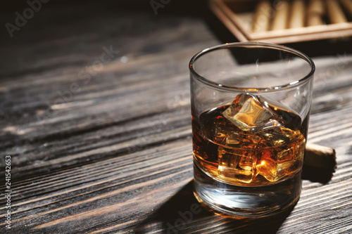 Glass of whiskey and cigar on wooden table